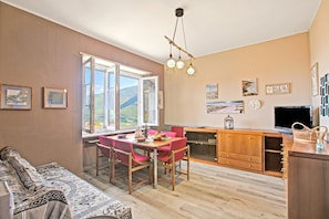 A modern kitchen with a dining area, wooden cabinets, a large window, and a view of the outdoors.