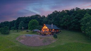 A large, single-story house with a wrap-around porch and a stone chimney, surrounded by a well-maintained lawn and trees. - The perfect family retreat, hot tub, fire pit, playhouse for the kids with a zip line! Plenty of fun for the young and old alike! All while enjoying the majestic views of Juniata County. (Honey Grove)