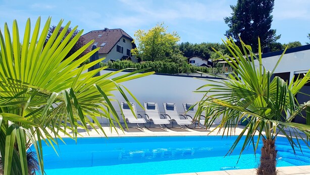 Ein Pool mit Liegestühlen, Palmen und Häusern im Hintergrund.