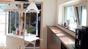 Eine moderne Küche mit einem weißen Esstisch, einer schwarzen Pendelleuchte und einem Fenster mit Vorhängen.