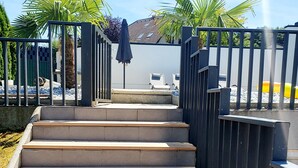 Betonstufen führen zu einem Poolbereich, umgeben von einem Metallzaun und Palmen.