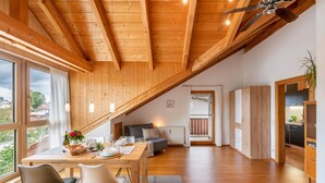 Un loft spacieux avec de hauts plafonds, des poutres apparentes, un coin repas avec des chaises, un canapé et une vue dégagée grâce à de grandes fenêtres.
