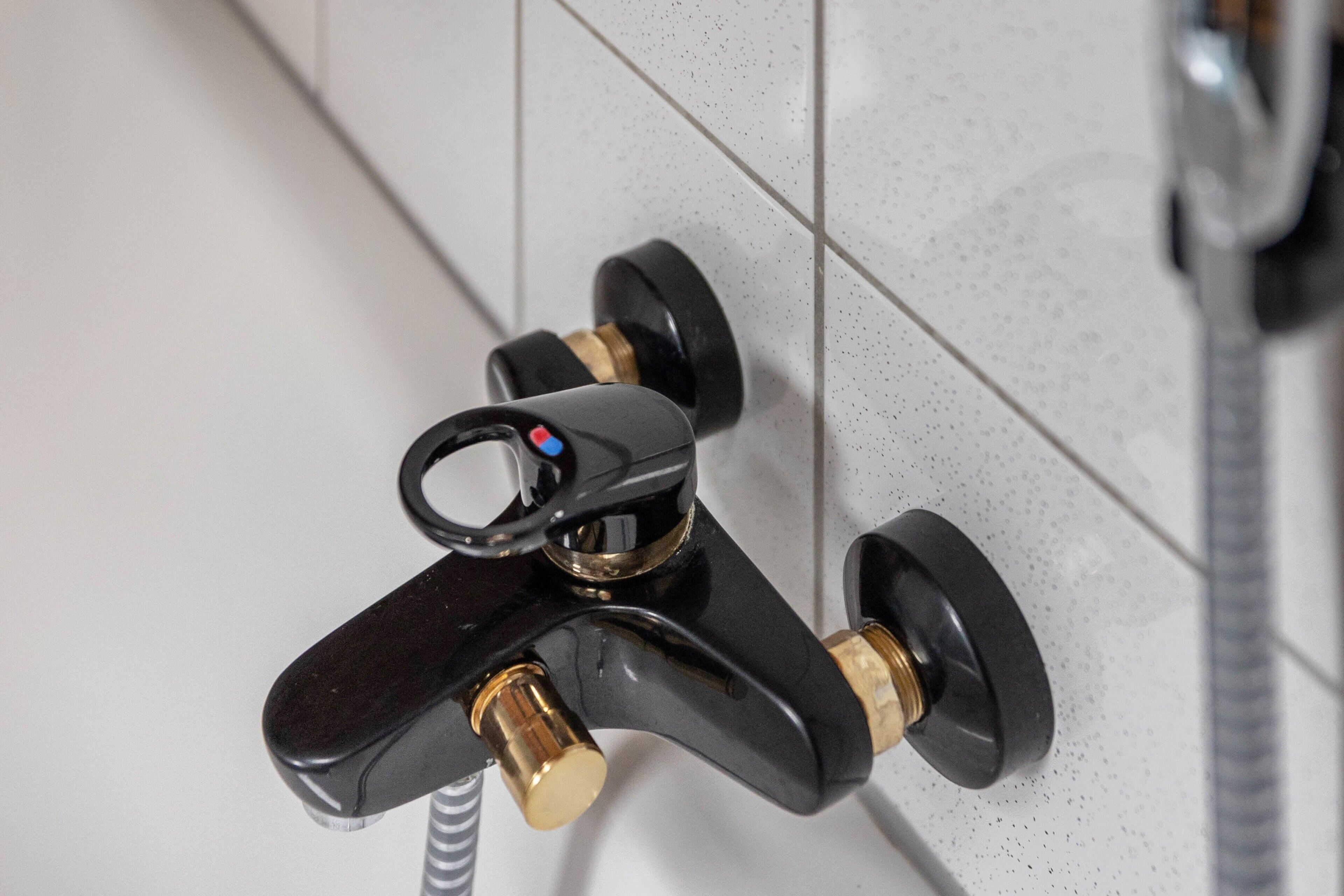 Un grifo negro con una palanca y una válvula de bronce, instalado en una pared de azulejos.