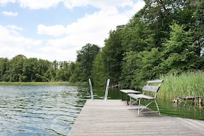 Eine Holzstele führt in einen stillen See, umgeben von üppiger Vegetation und Bäumen.