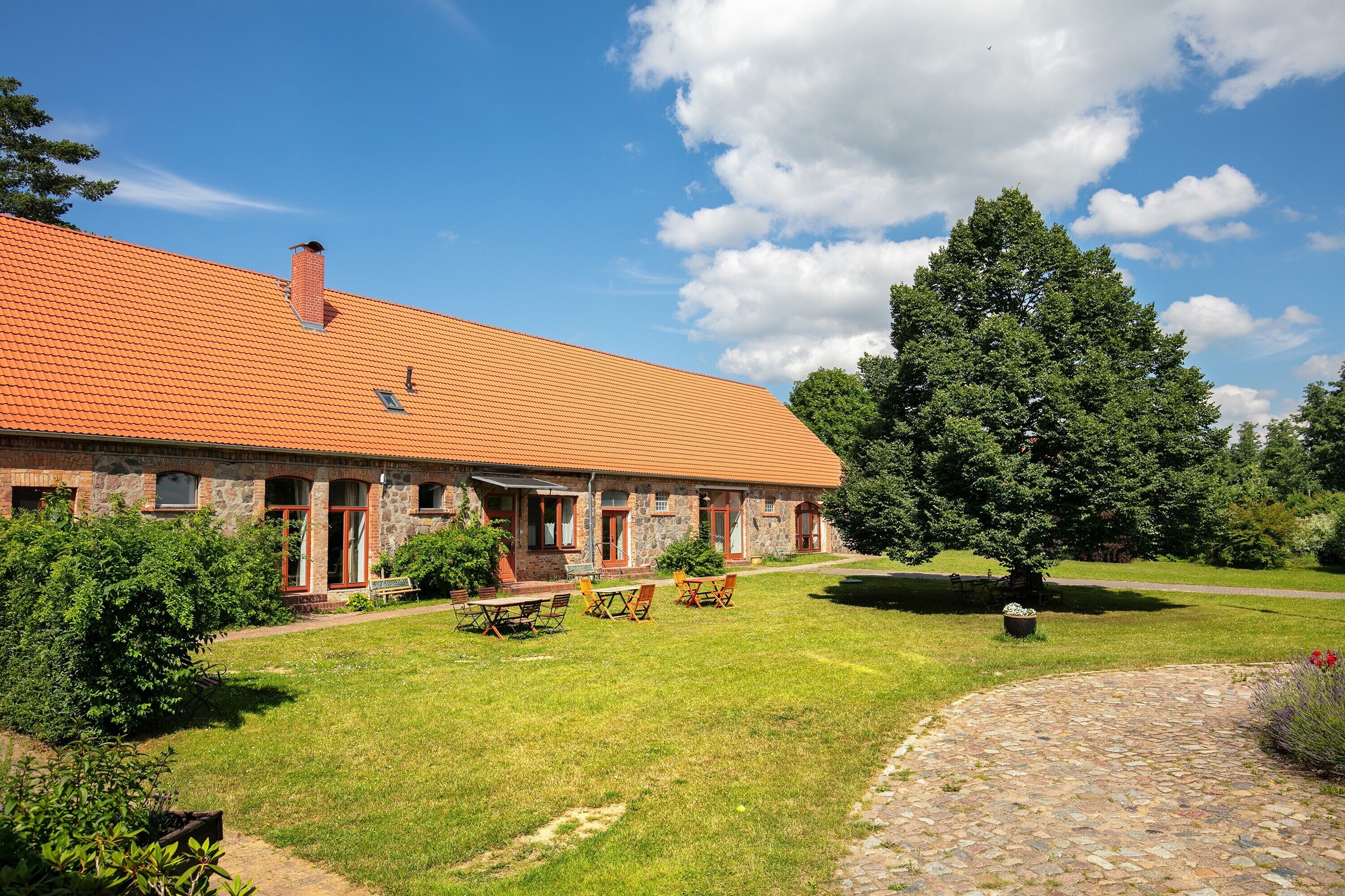 A stone building with a tiled roof, a paved driveway, and a well-maintained lawn with outdoor seating.