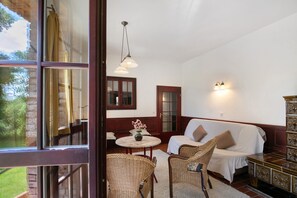 A room with a bed, two wicker chairs, a small table with a vase, a cabinet, and a window with curtains.
