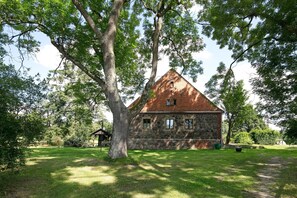 A stone building with a sloped roof, surrounded by trees and a grassy area.