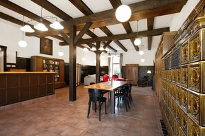 Quarto amplo com mesa de jantar de madeira, cadeiras pretas, balcão de recepção de madeira e um grande painel decorativo dourado.