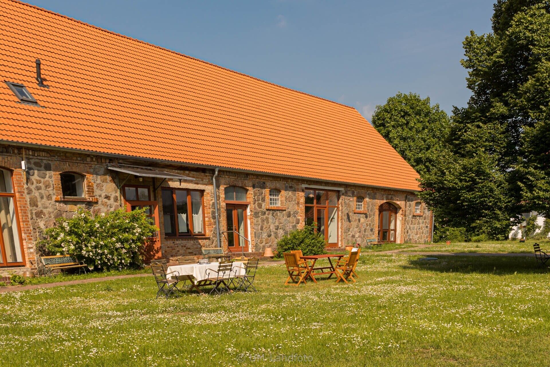 A stone building with a tiled roof, outdoor seating, and a grassy area.