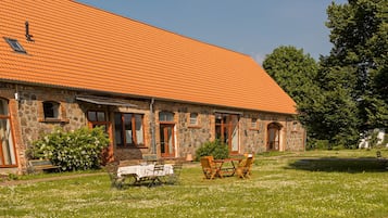 A stone building with a tiled roof, outdoor seating, and a grassy area.