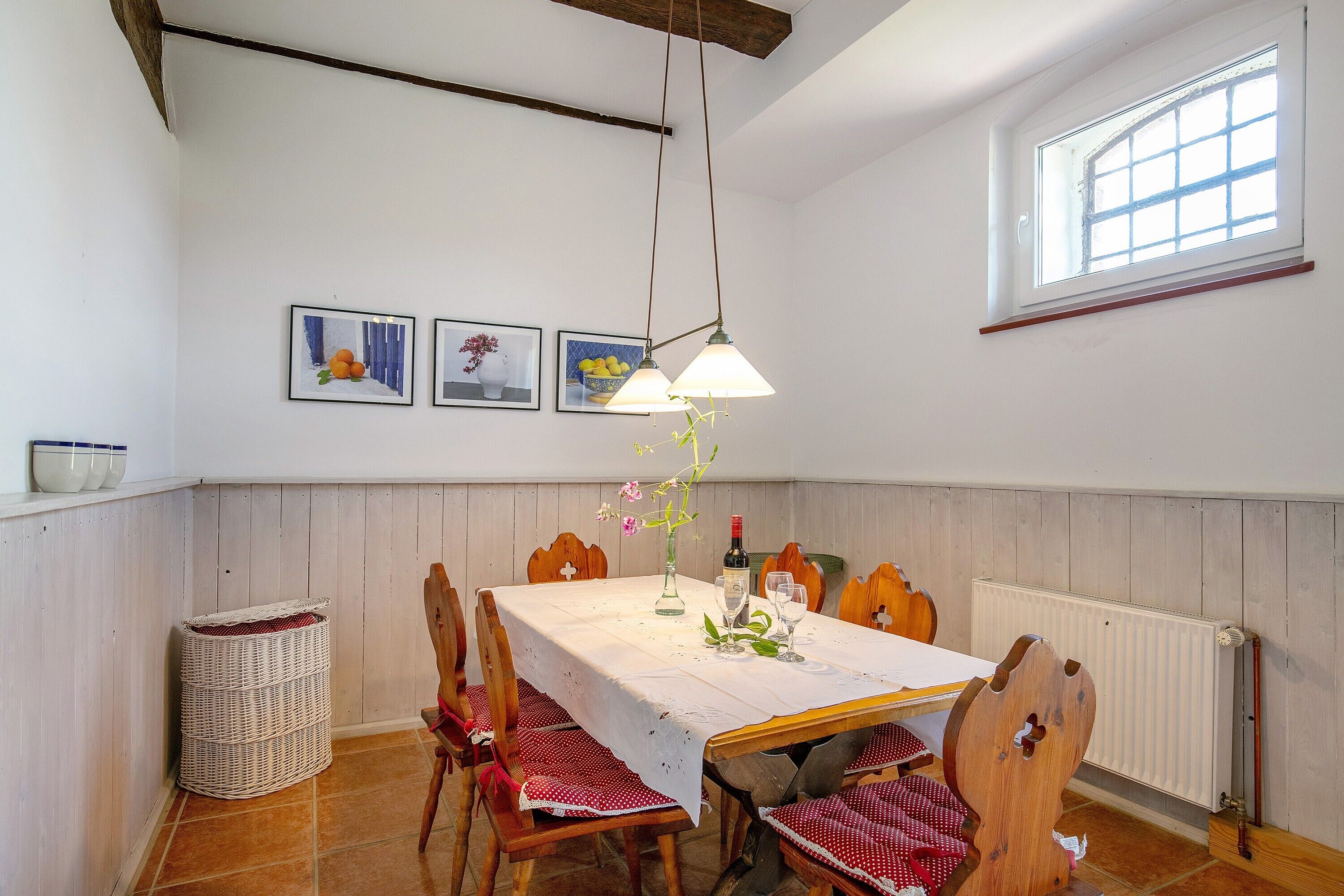 Een eethoek met een tafel voor vier personen, houten stoelen, een hanglamp en een raam met uitzicht.