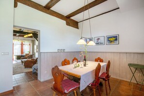Un coin repas avec une table dressée pour quatre personnes, des chaises en bois, un vase rempli de fleurs et un tableau accroché au mur.