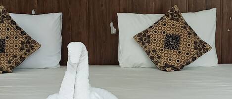 A hotel room with a wooden headboard, a bed with white bedding, two patterned pillows, and a colorful abstract painting on the wall.