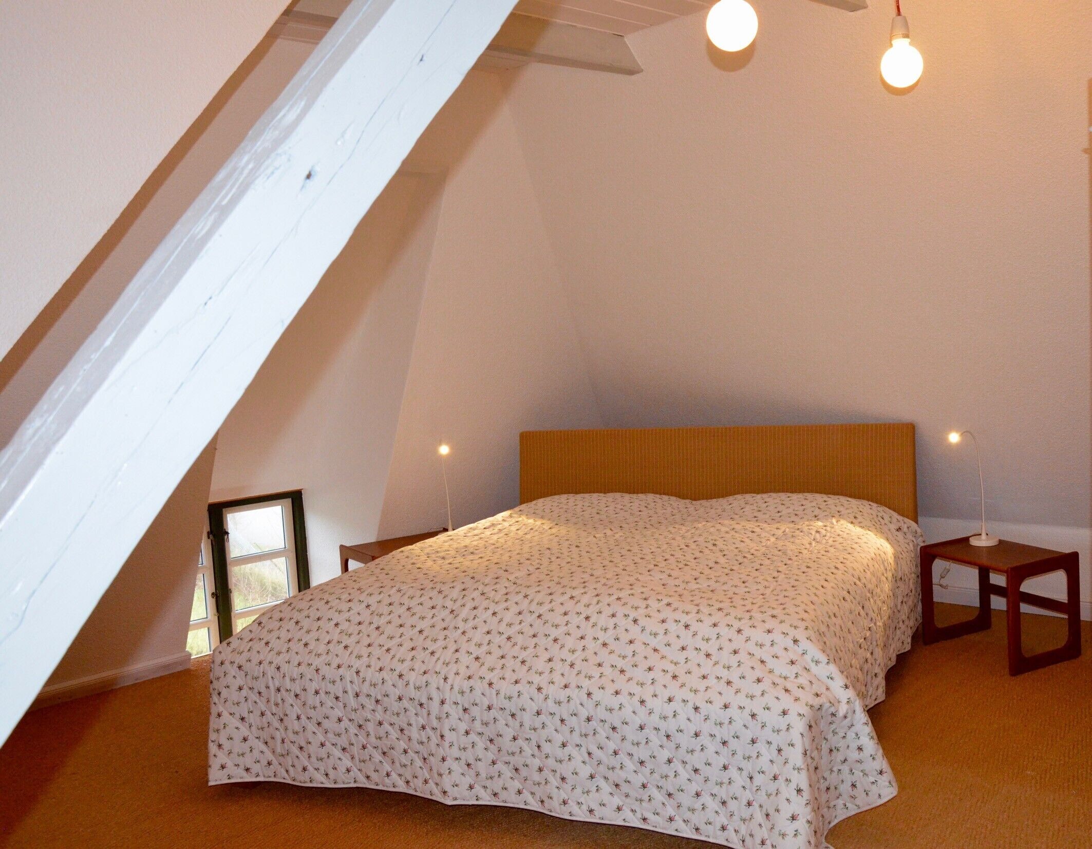 Une chambre à coucher avec un plafond en pente, un lit recouvert d’une couvre-lit à motifs, deux lampes de chevet et une table de chevet.