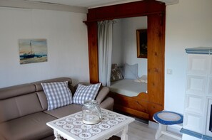 En stue med en sofa, ternede puder, et glas på et mønstret bord, en trædør og et hvidt skab.