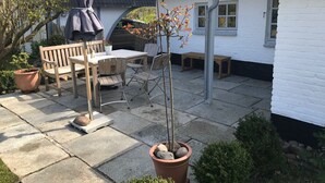 Une terrasse avec une table et des chaises, une plante en pot et un bâtiment à l’extérieur blanc.