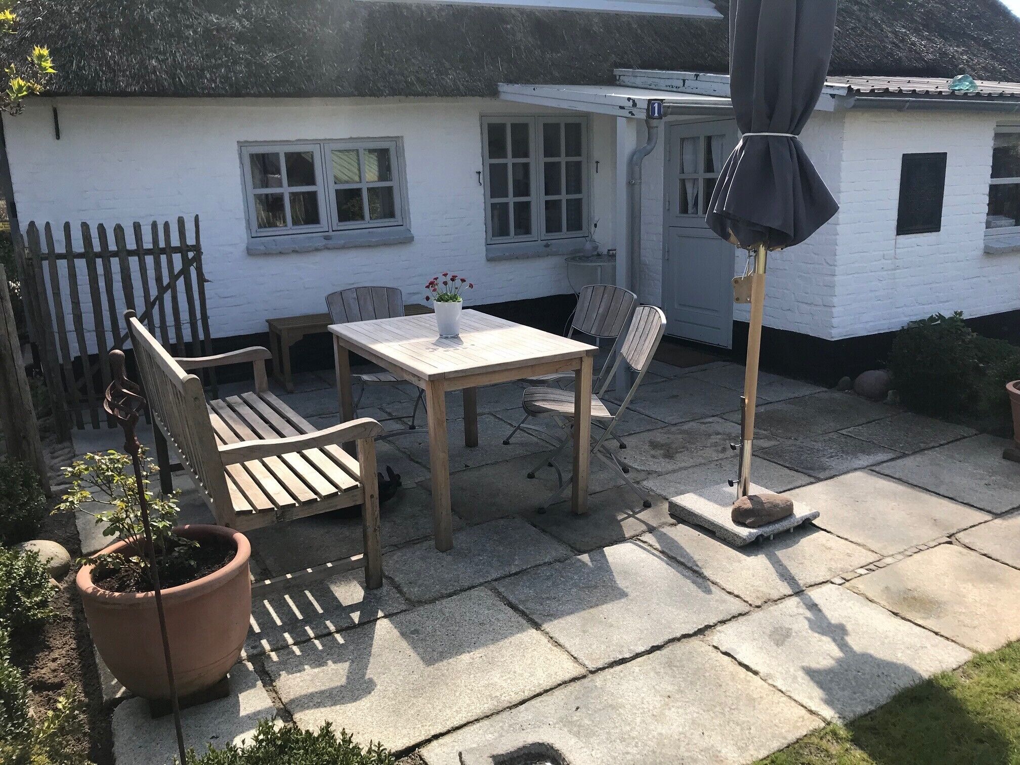 Une terrasse avec une table et des chaises, un pot de fleurs et un petit abri de jardin.