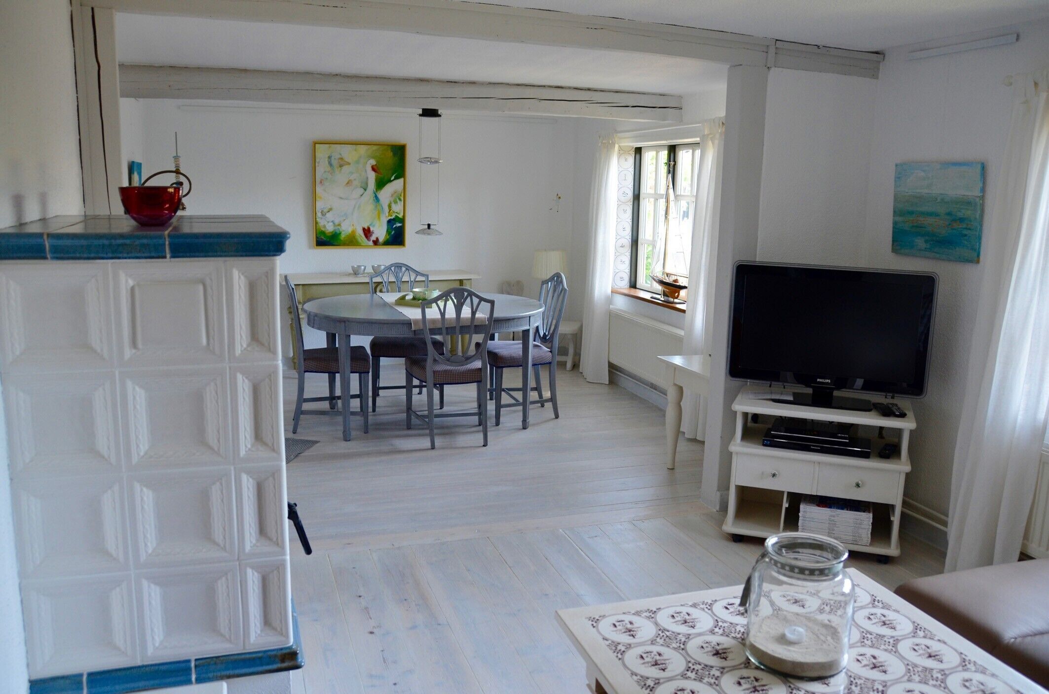 Een kamer met een eettafel, stoelen, een televisie en een raam.