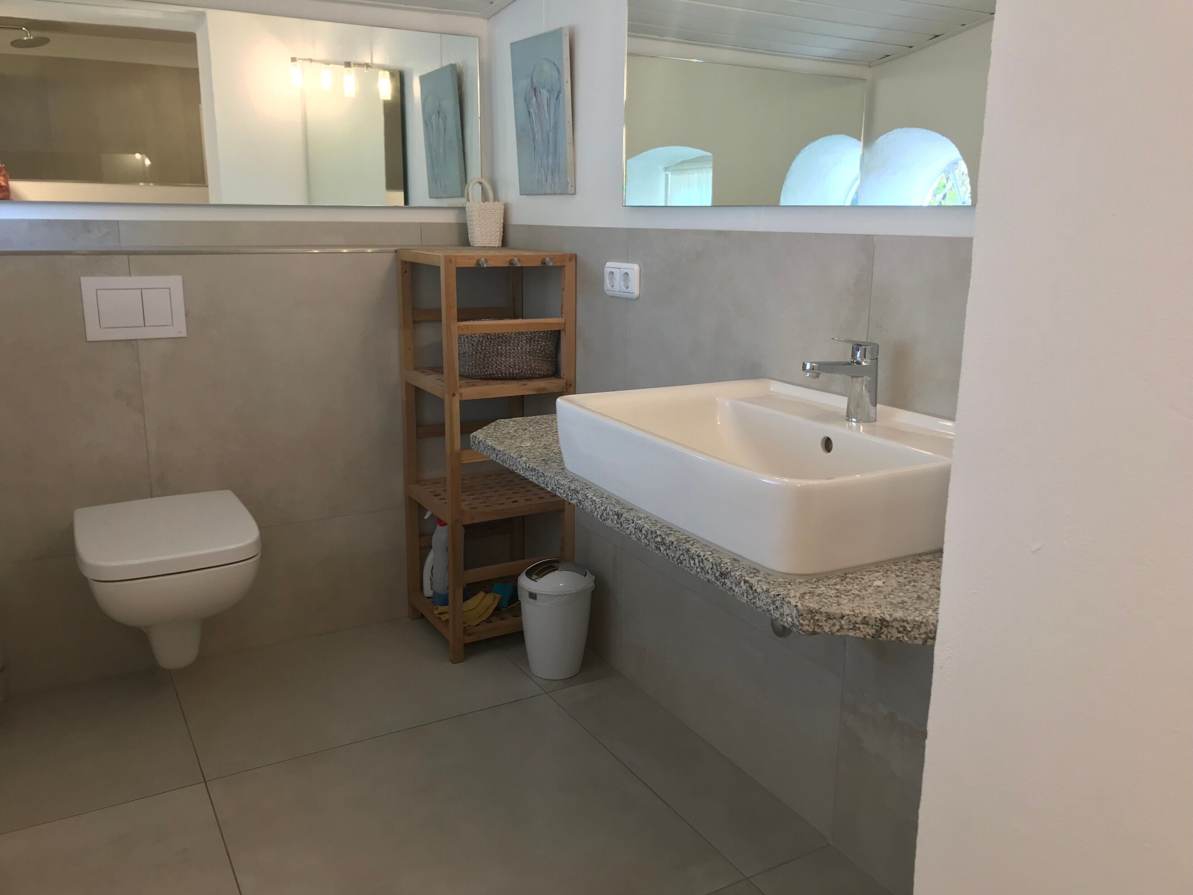 A bathroom with a toilet, a wooden shelf with baskets, a sink, and a mirror.