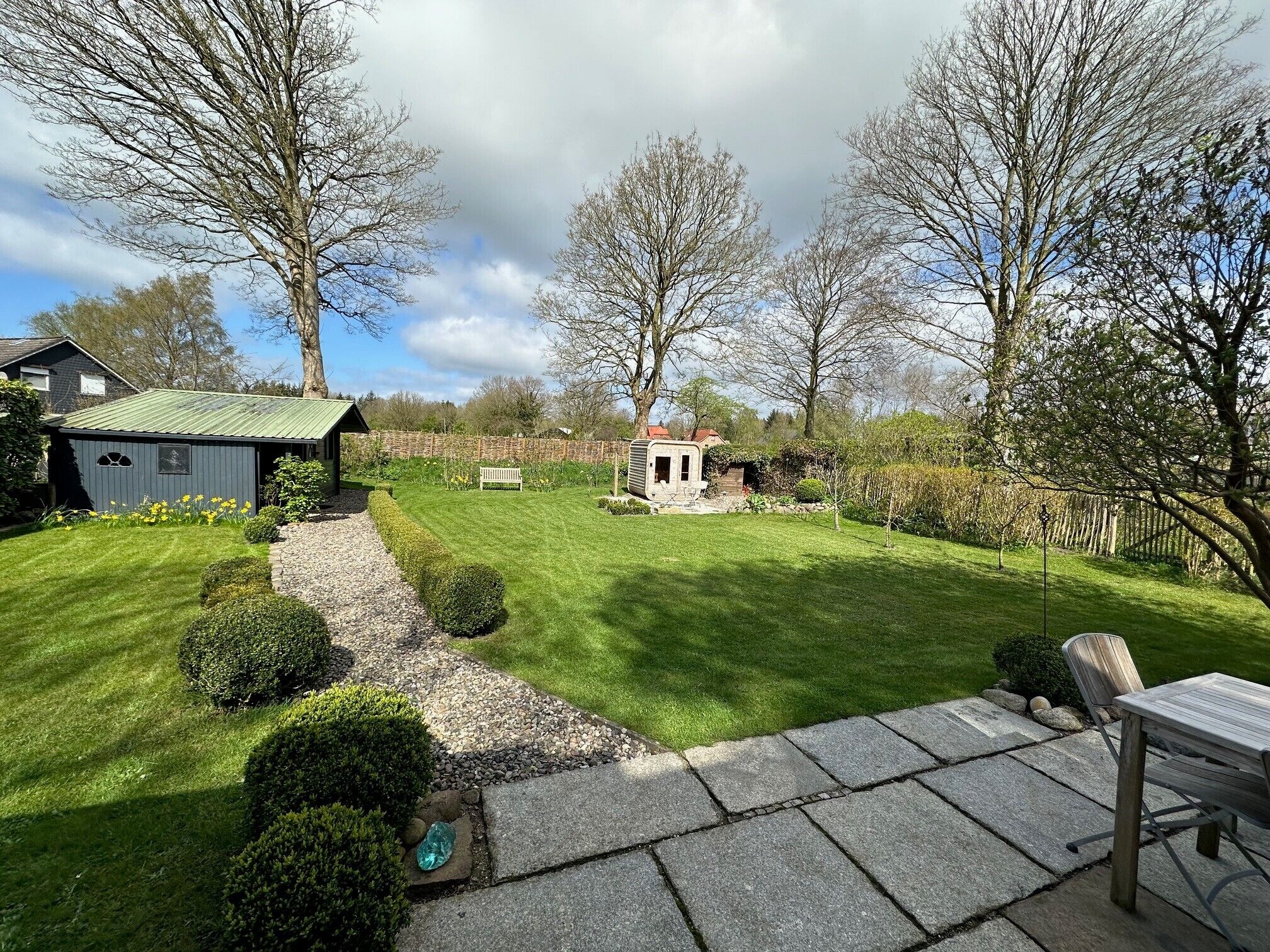 Een verzorgde tuin met gazon, een tuinhuisje, een bank en een terras.
