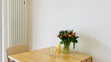 Ein Essbereich mit einem Holztisch, zwei Stühlen, einer Blumenvase, einer Kerze und einem Poster an der Wand.