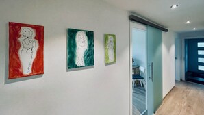 Un pasillo con tres obras de arte colgadas en la pared, una puerta corredera de vidrio que da a otra habitación, y suelo de madera.