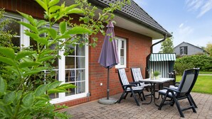 Eine Terrasse mit Tisch und Stühlen, einem lila Sonnenschirm und einem Ziegelhaus mit Fenster.