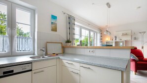 Eine moderne Küche mit weißen Schränken, einem Geschirrspüler, einer Spüle und einem Fenster mit Vorhängen.