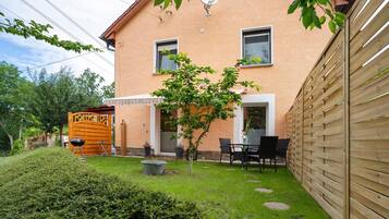 Een tweelaags huis met een terras, een houten hek en een kleine boom.