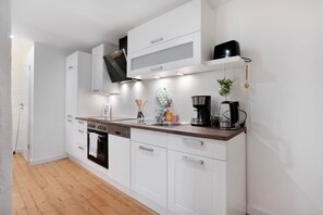A modern kitchen with white cabinetry, a wooden countertop, a built-in oven, and a coffee maker.