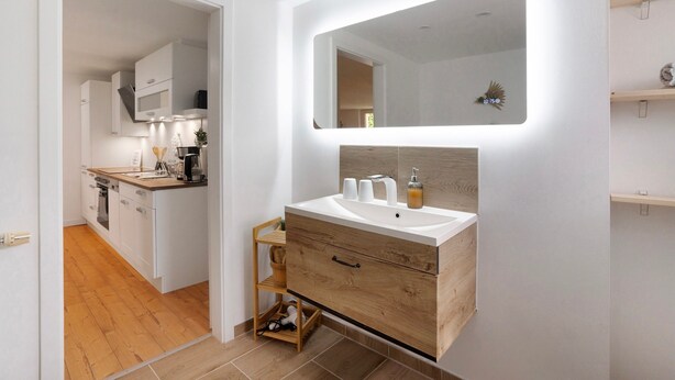 A modern bathroom with a wooden vanity, a large mirror, and a built-in sink. - Apartment 'Grünzweig' with Private Terrace by the Water (Oelsnitz/Vogtl.)