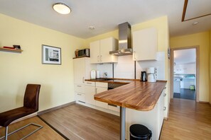 A kitchen with a wooden countertop, white cabinets, a microwave, a stove, and a sink.