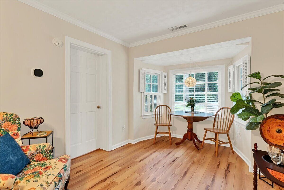 Una habitación con piso de madera, un sofá floral, una mesa de comedor con sillas y una ventana con persianas.
