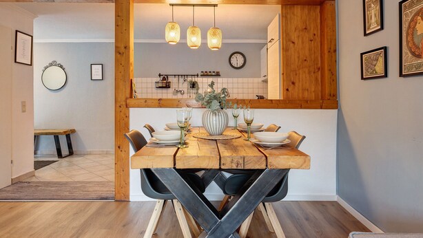A dining area with a wooden table, chairs, and hanging pendant lights. - Apartment 'Romantische Whg In Ruhiger Lage' with Private Garden and Wi-Fi (Stelle)