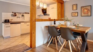 A modern kitchen with white cabinets, a wooden dining table, and a black chair. - Apartment 'Romantische Whg In Ruhiger Lage' with Private Garden and Wi-Fi (Stelle)