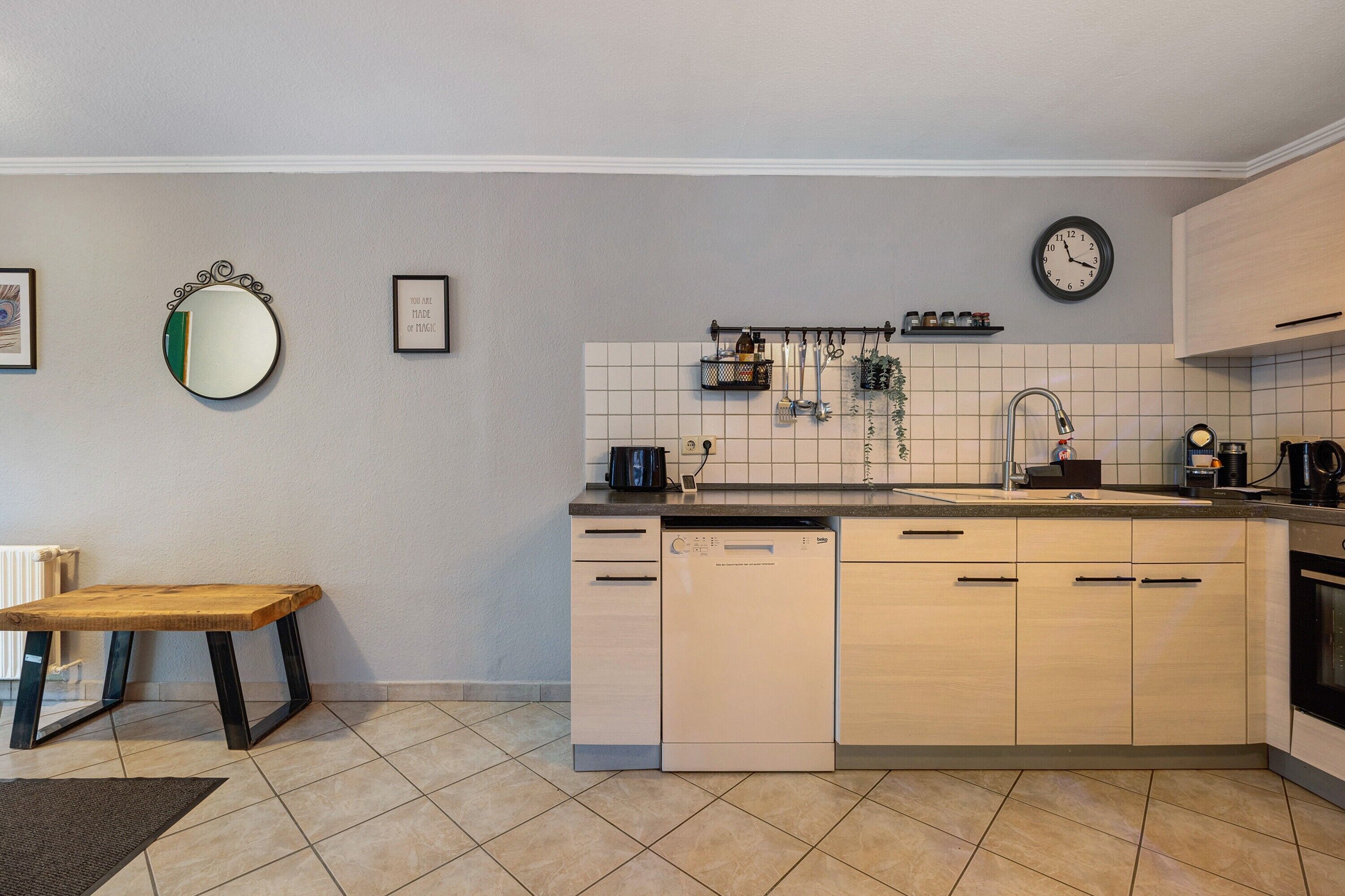 Une cuisine équipée d’un lave-vaisselle, d’un évier, d’une horloge et d’un miroir au mur.