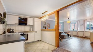 A modern kitchen with a built-in oven, a dining area with a table and chairs, and a view of the living room through an open doorway. - Apartment 'Romantische Whg In Ruhiger Lage' with Private Garden and Wi-Fi (Stelle)
