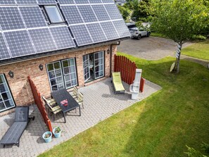A house with solar panels on the roof, a patio with a table and chairs, and a lawn.
