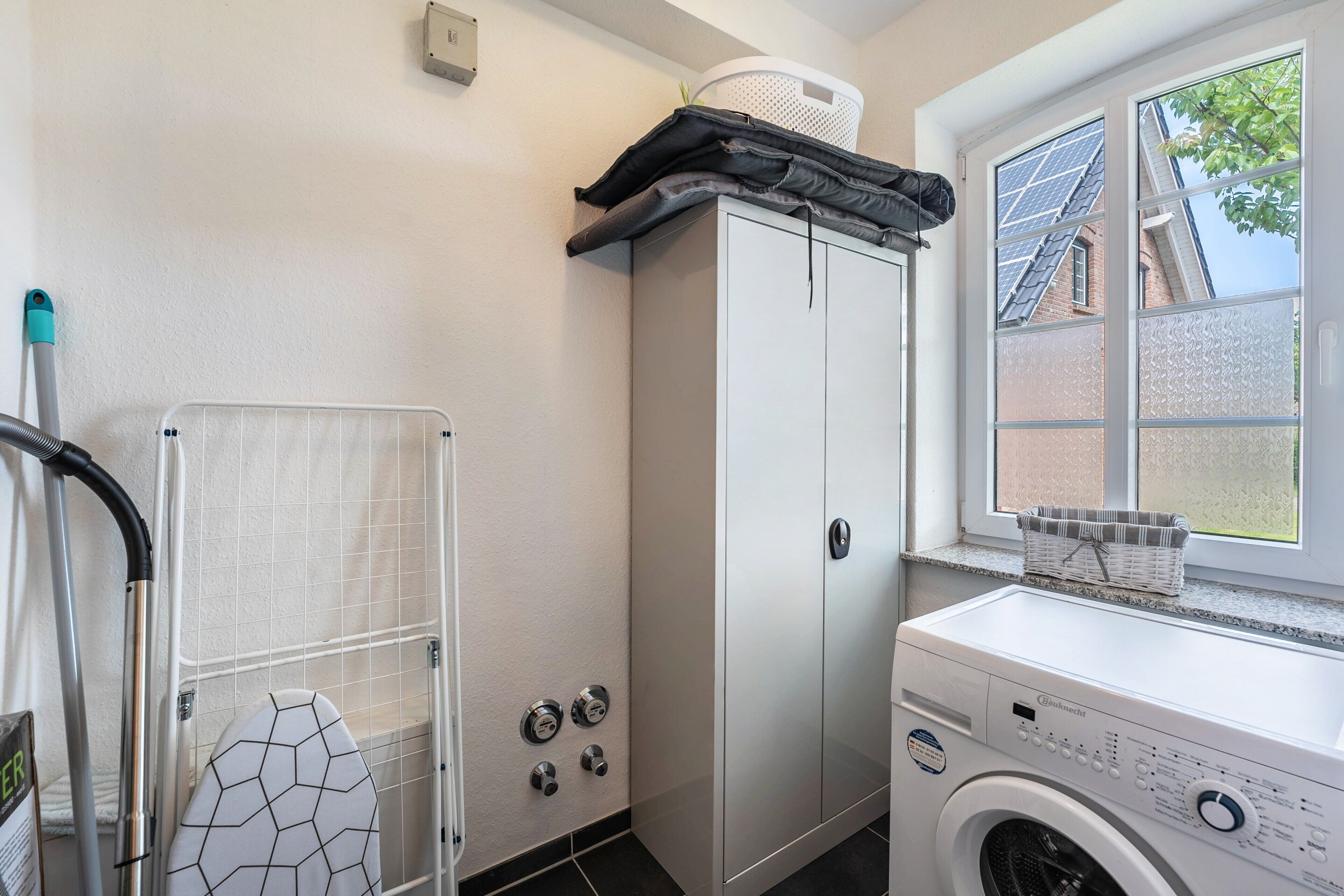 A laundry room with a washing machine, a drying rack, and a window with solar panels.