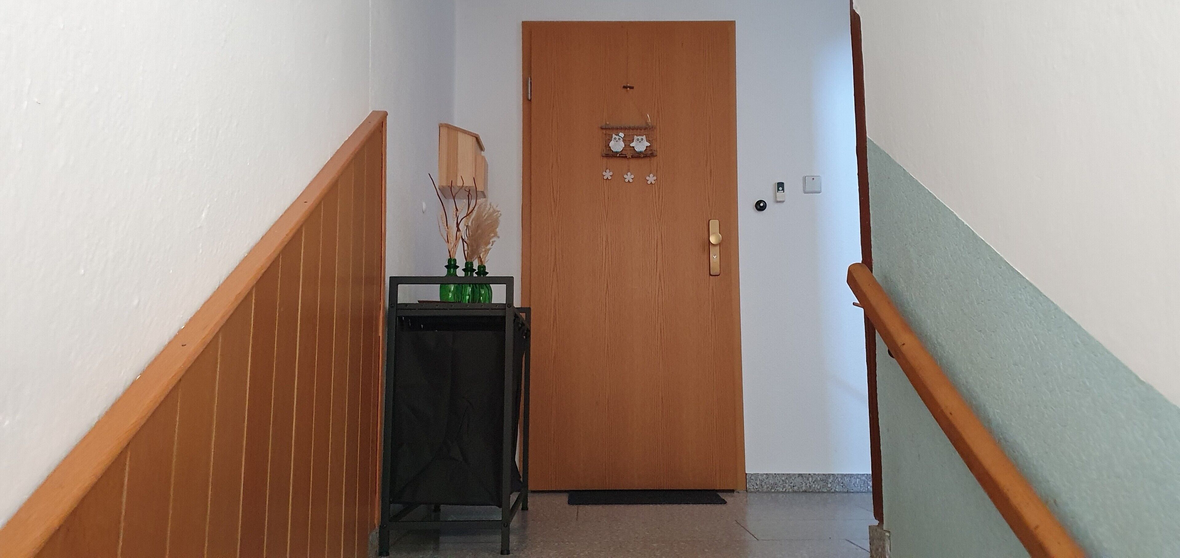 Un couloir avec une porte en bois, une petite table sur laquelle est posé un vase, et un escalier.