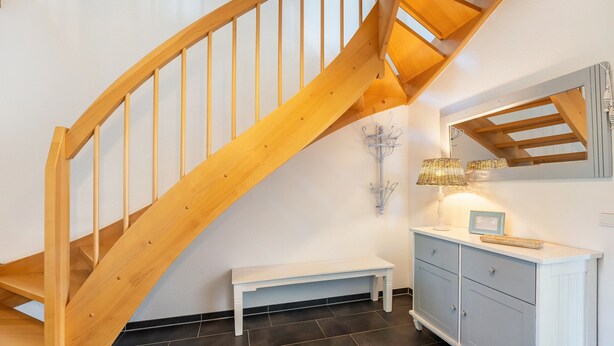 A wooden staircase, a white bench, a cabinet with drawers, and a wall-mounted lamp.