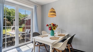A dining area with a white table, chairs, a hanging light, and a vase with flowers.