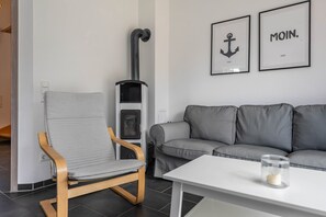Un salon moderne avec un canapé gris, une chaise en bois, une table blanche et une cheminée.