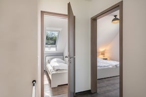 A bedroom with a skylight, a bed, a bedside table with a lamp, and a door leading to another room.