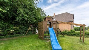 A wooden play structure with a blue slide, a climbing wall, and a small house-like pavilion in a grassy backyard.