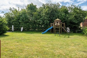 A wooden play structure with a slide in a grassy backyard.