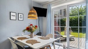 Ein Essbereich mit Tisch, Stühlen, einem Fernseher und Blick auf den Garten.