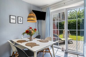 A dining area with a table, chairs, a TV, and a view of the garden.