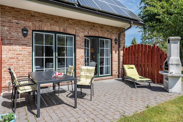 A brick house with a patio, a table with chairs, a lounge chair, and a barbecue grill.