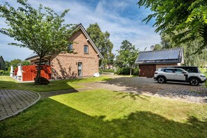 A brick house with a paved driveway, a red fence, and a parked car.